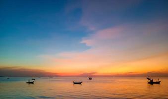 Sky and sea at sunset, local boats floating in the middle of the sea, orange and blue sky reflecting the sea, giving a calm feeling. photo