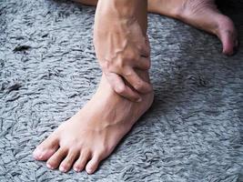 mujer asiática usa masaje manual en la pierna con dolor de tobillo y esguince foto