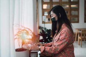 joven asiática con mascarilla trabajando en una laptop mientras está sentada en un café. chica joven que trabaja con la computadora portátil. concepto de coronavirus covid-19. foto