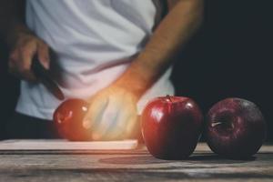 Man hand holding knife prepare to cut red apple on wood table and dark background. Fruits and food concept. photo