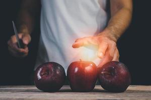 Man hand holding knife prepare to cut red apple on wood table and dark background. Fruits and food concept. photo