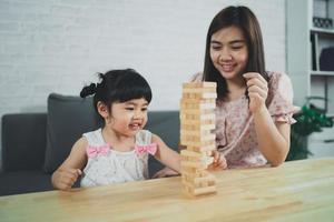 concepto de juegos de jenga. hija y madre asiáticas sonriendo alegremente y riendo jugando juegos de jenga de madera sentados en un sofá en la sala de estar en casa, actividades familiares de madre e hija jugando juegos felices foto