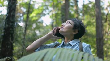 Woman nature explorer using mobile smartphone talking to her family while trekking in the forest. video