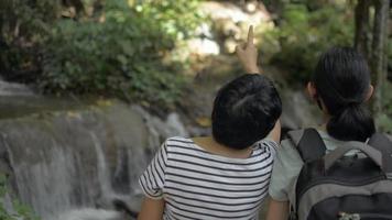 la vista lateral trasera de la madre y su hija adolescente disfrutan mirando el hermoso paisaje de la cascada. video