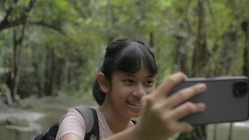 Pretty girl taking on video live streaming with smartphone in the jungle with water stream.