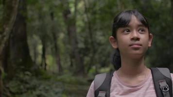 Portrait hübsches Mädchen mit Rucksack, das sich umsieht, während es im tropischen Regenwald erkundet.