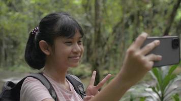 Girl enjoy taking a selfie with smartphone while posing near a creek in tropical forest. video