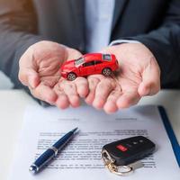 Businessman hand holding red car toy with vehicle keyless, pen and contract document. buy and sale, insurance, rental and contract agreement concepts