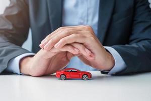 Businessman hand cover or protection red car toy on table. Car insurance, warranty, repair, Financial, banking and money concept photo