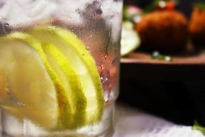 Close up photo of cold infused water with lemon slices in a clear glass, and visible outside the glass