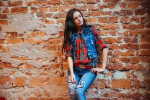 Beautiful young woman stands near the old brick wall. Youth styl