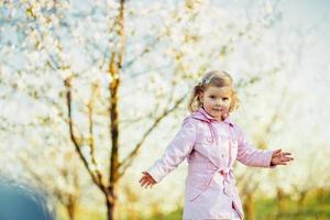 pequeña niña de 3 años, que corre entre árboles en flor fuera foto