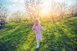 Little baby girl that runs between flowering trees at sunset. Ar photo