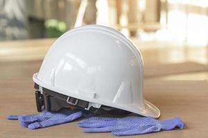 casco de seguridad blanco y guantes azules en el suelo de madera.