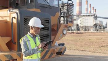 Senior Asian engineer in safety clothing Wear a white hard hat and use a tablet in front of a large truck