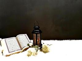 The lantern of Ramadan is black in color, luminous, decorated with wooden motifs, next to the Holy Quran, with a few white roses