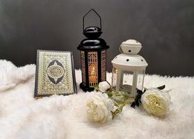 The lantern of Ramadan is black in color, luminous, decorated with wooden motifs, next to the Holy Quran, with a few white roses photo