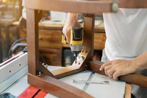 carpenter repair chair and using electric screwdriver at workshop, furniture restoration woodworking concept. selective focus photo