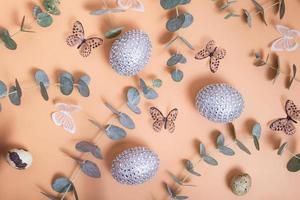 Pattern of Easter eggs, eucalyptus, butterflies and beads. Trendy flat lay composition on color background photo