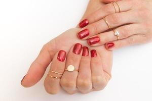 Manicure gel polish of red color with sparkles on female hands with rings photo