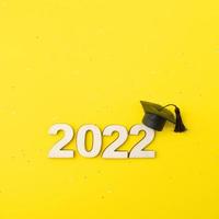 sombrero o gorra graduados con el número de madera 2022 sobre un fondo de brillo amarillo. concepto de clase 2022 foto