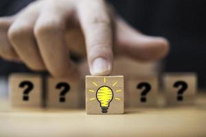 Hand pushing lightbulb drawing which print screen on wooden cube block among human and question mark for creative thinking idea and problem solving concept. photo