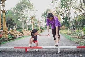 Asian mother and her daughter as they stretching their legs before they go for a run at the park. Sport family concept photo