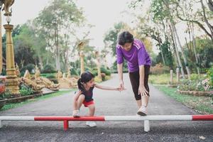 madre asiática y su hija mientras estiran las piernas antes de ir a correr al parque. concepto de familia deportiva foto