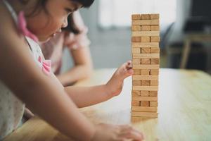 hija asiática y madre sonriendo alegremente y riendo jugando torre de juguete de madera sentada en un sofá en la sala de estar en casa, actividades familiares de madre e hija jugando juegos felices foto