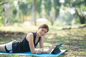 Asian fitness woman doing a yoga according to a video clip. Asian woman using tablet and doing yoga in park photo