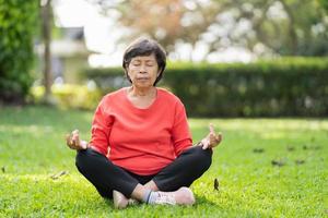 Senior asian woman practicing yoga lesson, breathing, meditating in garden. Half Lotus pose with mudra gesture, working out, Well being, wellness concept photo