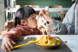 madre alimentando a su hija. niña feliz comiendo helado con su madre en la sala de estar. concepto de niño pequeño de comida feliz familiar foto