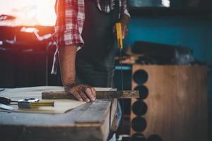 carpintero de edad avanzada que usa sierra trabajando en artesanía de madera en el taller para producir material de construcción o muebles de madera. foto