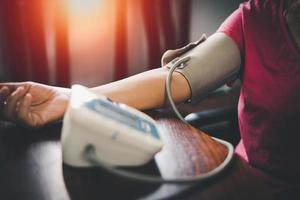 Elder woman upper arm bicep in cuff. Older retired lady measuring manually blood pressure, using digital tonometer machine at home. Healthcare, disease treatment concept. photo