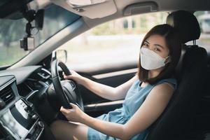 Happy asian woman wearing surgical mask while driving car. During covid-19 pandemic wearing a mask when you driving car go to outside leaving home. photo