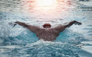 Nadador deportivo con gorra respirando realizando el estilo mariposa. nadador nadando en la piscina. concepto de natación deportiva. foto