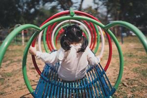 Cute asian girl play on school or kindergarten yard or playground. Healthy summer activity for children. Little asian girl climbing outdoors at playground. Child playing on outdoor playground. photo