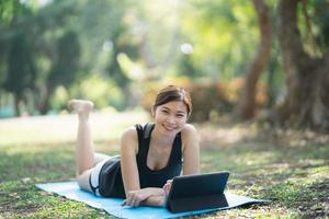 Asian fitness woman doing a yoga according to a video clip. Asian woman using tablet and doing yoga in park photo