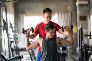 deportista asiático en forma haciendo ejercicio en la sala de pesas con entrenador en el gimnasio. concepto de hombre deportivo foto