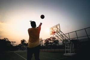 silueta de jugador de baloncesto al atardecer. jugador de baloncesto dispara un tiro. concepto de baloncesto deportivo. foto