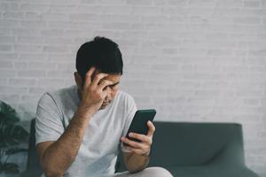 Depression concept. Asian man sad and checking mobile phone sitting on the sofa in the living room at home, Asian man serious and worry while using mobile phone. photo