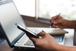 young man using  laptop computer and  mobile phone When looking for financial information in business, work at the desk. Writing with a pen, studying remotely from home and working from home. photo