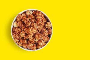 Chocolate caramel sweet popcorn in white bowl isolated on yellow background with clipping path. Top view. photo