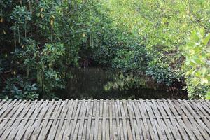 mesa de bambú vacía frente al canal en el fondo del bosque. se puede utilizar para exhibición o producto de montaje. terraza de madera del restaurante en el jardín. foto