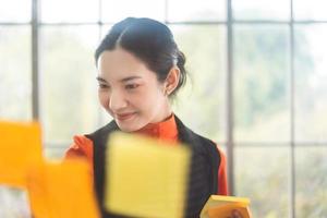 Asian woman write post it on glass board. photo