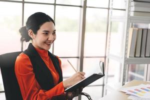 Young adult asian business woman writing on diary book at office on day photo