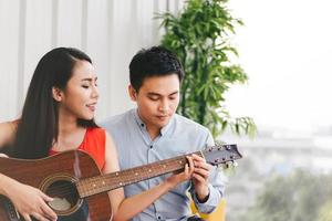 Man teaching how to play guitar to girlfriend at home on day photo
