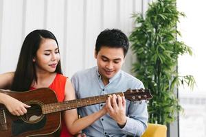 pareja asiática romántica tocando la guitarra juntos. Actividad sencilla en casa. foto