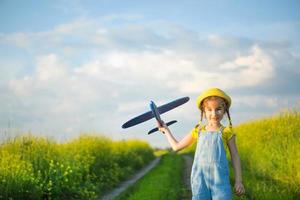 Girl in a yellow panama hat launches a toy plane into the field. Summer time, happy childhood, dreams and carelessness. Air tour from a travel agency on a trip, flight, adventure and vacation.