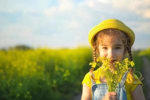 una niña en un campo de verano amarillo huele un ramo de flores. día soleado, vacaciones, alergia a la floración, libertad. cultivo de colza agrícola, trigo sarraceno. copie el espacio